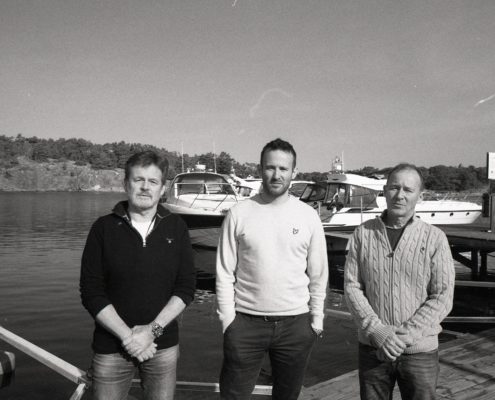 Tre män står bredvid varandra vid en hamn